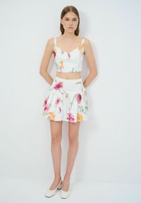 Blumiges Zweiteiler-Outfit mit einem Cropped-Top und einem plissierten Rock. Weiße Basis mit bunten Blumenmustern. Glatte Stofftextur.