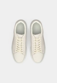 Ζευγάρι καθαρών, εκρού σουέντ αθ�λητικών παπουτσιών με κρέμ κορδόνια, απεικονιζόμενο από πάνω σε ένα απλό λευκό φόντο.