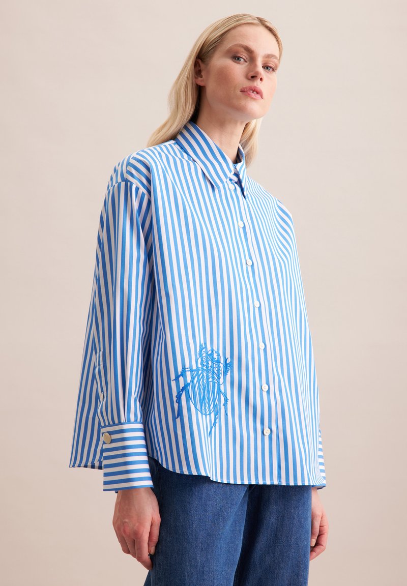 Camicia a righe blu e bianche dal taglio rilassato, con maniche lunghe, collo a punta e un coleottero ricamato sul davanti.