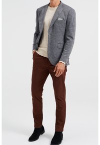 Grå hundtandsmönstrad kavaj över en krämfärgad tröja, matchad med bruna byxor och svarta ankelstövlar. Kavajen har en fickduk.