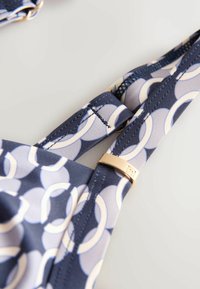 Gros plan sur une sangle en tissu motif marine et gris avec anneau métallique réglable sur fond blanc.