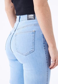 Light blue denim jeans with a high waistband and two back pockets. Features the DRDENIM brand tag on the waistband. Smooth texture.
