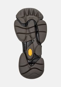 Suola Vibram in grigio scuro, caratterizzata da modelli testurizzati e scanalature per la presa. Logo Vibram giallo ben visibile vicino al centro.
