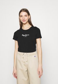 T-shirt noir en coton à manches courtes, avec le texte blanc "Pepe Jeans LONDON" sur le devant. Assorti avec un pantalon beige à cordon de serrage.