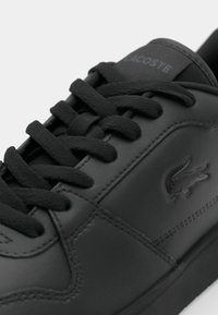 Baskets en cuir noir avec lacets noirs, logo crocodile Lacoste embossé sur le côté et marquage "LACOSTE" sur la languette.