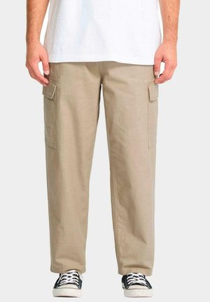 Pantalones cargo color caqui fabricados en algodón, con dos bolsillos laterales, corte relajado y diseño de pierna recta, usados con zapatillas negras.