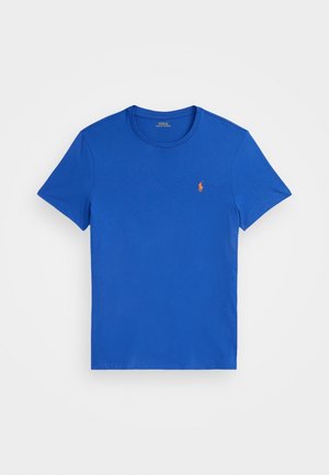 Niebieska koszulka z krótkim rękawem i okrągłym dekoltem, z małym pomarańczowym logo Polo Ralph Lauren po lewej stronie na białym tle.