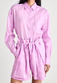 Light pink linen button-up shirt with a chest pocket, paired with matching high-waisted shorts featuring a gathered waistband and side pockets.