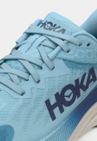 Svetlo modrá športová obuv s textúrovaným zvrškom, šnúrkami a tmavomodrým brandingom "HOKA". Obsahuje odolnú podrážku s vlnovým vzorom.