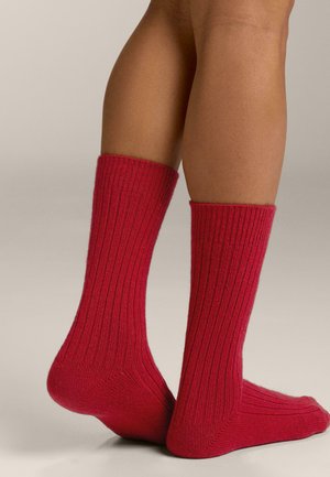 Șosete roșii cu model nervurat, cu design la jumătatea gambei, textură tricotată și toc și vârf întăriți. Materialul pare moale și elastic.