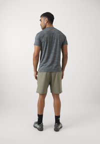Grå stribet t-shirt, kortærmet, parret med lysegrønne shorts. Modellen har sorte sokker og grå løbesko på. Minimalistisk design.