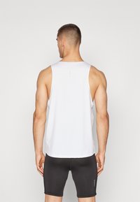 Hvid ærmeløs atletisk tanktop med rund halsudskæring og glat stof. Modellen har sorte tætsiddende shorts på. Bagfra viser den rene linjer.