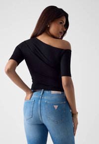 Czarna bluzka z odkrytymi ramionami i krótkimi rękawami, zestawiona z jasnoniebieskimi dżinsami z czerwoną metką z logo na tylnej kieszeni.