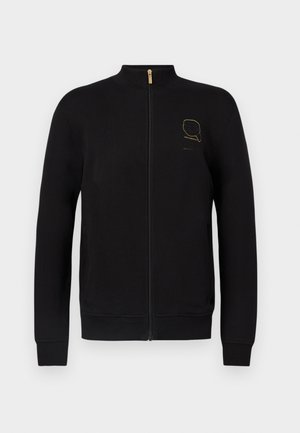 Melns džemperis ar rāvējslēdzēju un augstu apkakli, izgatavots no mīksta auduma. Uz krūtīm ir zeltiem rakstīts logotips, un piedurkņu gali un apakšējā mala ir ribota.