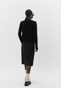 Czarny dziany kardigan z długimi rękawami, zestawiony z czarną sukienką midi. Strój cechuje się teksturowaną tkaniną oraz czarnymi butami i białymi skarpetkami.