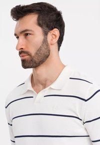 Polo bianco con righe orizzontali blu navy, colletto a costine e logo ricamato sul petto. Il tessuto sembra lavorato a maglia e texture.