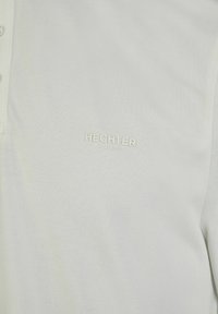 Weißes Polohemd aus atmungsaktivem Material, mit einem strukturierten Muster, kurzen Ärmeln und einem gestickten "HECHTER PARIS"-Logo.