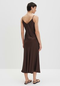 Bruine satijnen camisole top met dunne bandjes, gecombineerd met een bijpassende midi-rok. De outfit heeft een vloeiende uitstraling en een subtiele glans.