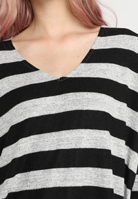 Gestreifter V-Ausschnitt-Oberteil mit abwechselnden schwarzen und grauen horizontalen Streifen, aus einem weichen, strukturierten Stoff gefertigt.