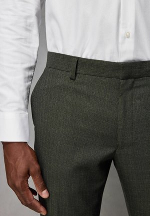 Mørkegrønne skræddersyede bukser med en subtil tekstur; flad front, slim fit og bæltestropper, parret med en hvid skjorte med knapper.