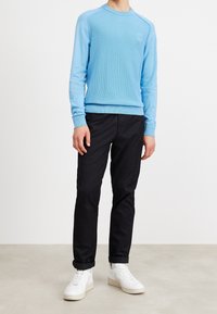 Hellblauer, strukturierten Pullover mit langen Ärmeln und Rundhalsausschnitt, kombiniert mit schwarzen Hosen und weißen Sneakern. Einfaches Design, keine sichtbaren Logos.