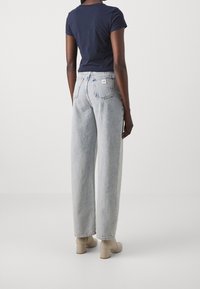 Námořnický top s krátkým rukávem v kombinaci s světle modrými kalhotami s vysokým pasem a volným střihem. Kalhoty mají zadní kapsy a jemné vyblednutí. Béžové boty na blokovém podpatku.