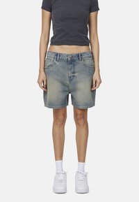 Shorts in denim di colore azzurro chiaro con una finitura slavata, dotati di cinque tasche, passanti per la cintura e un taglio dritto. Abbinati a sneakers bianche.