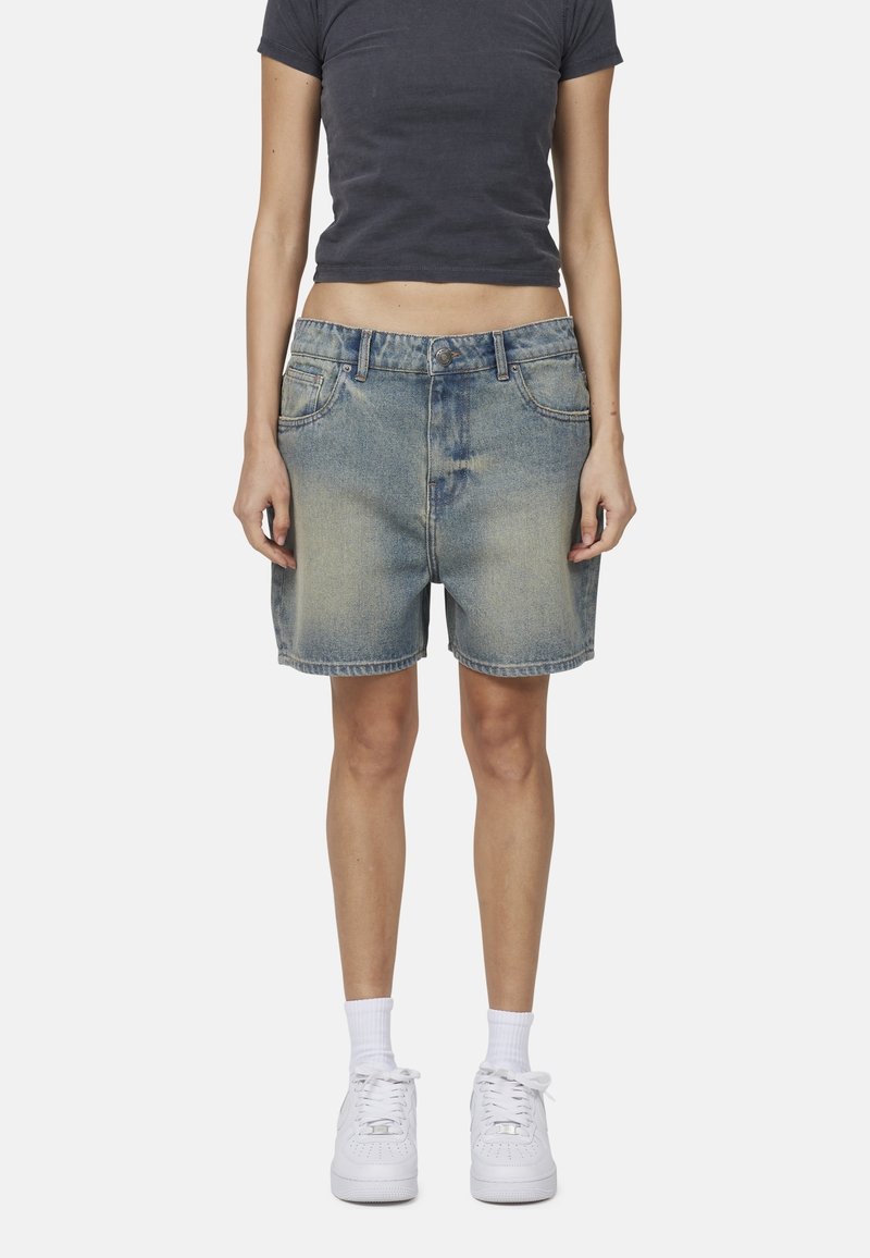 Shorts in denim di colore azzurro chiaro con una finitura slavata, dotati di cinque tasche, passanti per la cintura e un taglio dritto. Abbinati a sneakers bianche.