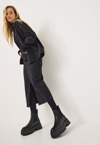 Chaqueta y falda de mezclilla negra combinadas con botas Chelsea de plataforma negras. El atuendo presenta líneas elegantes y una apariencia texturizada.