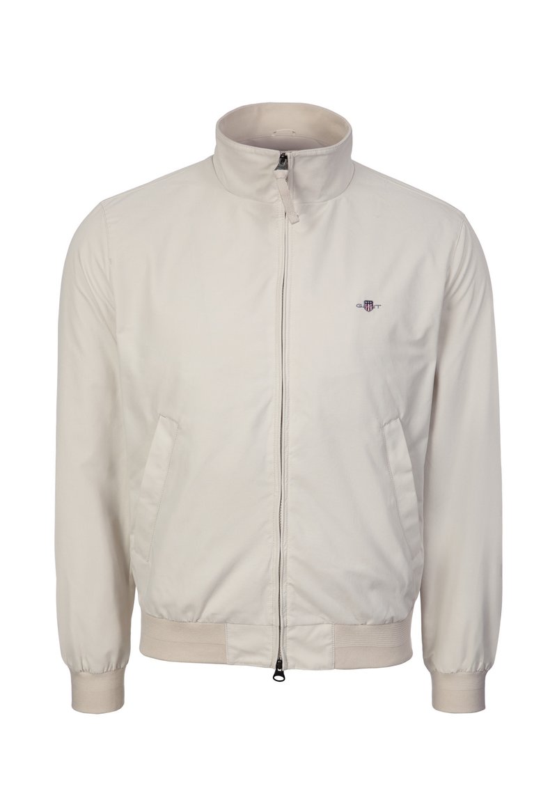 Giacca bomber beige con zip, collo alla coreana, polsini e orlo a costine, tasche laterali e piccolo logo ricamato sul petto a sinistra.