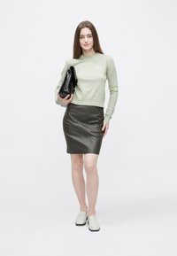 Vaaleanvihreä neulepusero, musta nahkainen kynähame ja harmaat liukusukat. Kantaa mustaa clutch-laukkua. Minimalistinen muotoilu, sileä tekstuuri.