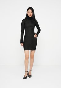 Μαύρο μίνι φόρεμα μακρύ μανίκι με εφαρμοστή γραμμή, που διαθέτει ανάγλυφο σχέδιο πλέγματος και καμπυλωτό στρίφωμα, συνδυασμένο με μαύρες ψηλές γόβες.