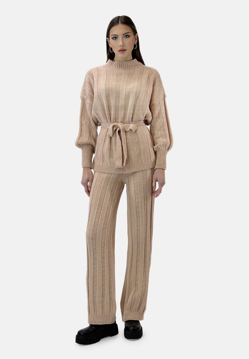 Dzianinowy zestaw w kolorze jasnego beżu; posiada ryflowaną teksturę, długie rękawy i pasek w talii na górze. Spódniczki w kształcie dzwonu z podobnym wzorem.