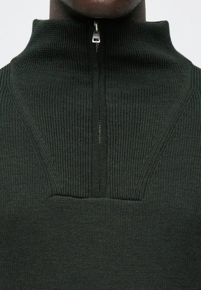 Σκούρο πράσινο, πλεκτό πουλόβερ με ραβδώσεις, ψηλό γιακά και κλείσιμο με μισή φερμουάρ. Διαθέτει υφή σχεδίασης και ραφές χωρίς ραφές στον λαιμό.
