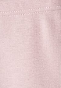 Tela de color rosa claro con una textura suave y elástica, que presenta un sutil patrón acanalado. La costura es visible a lo largo de un borde.