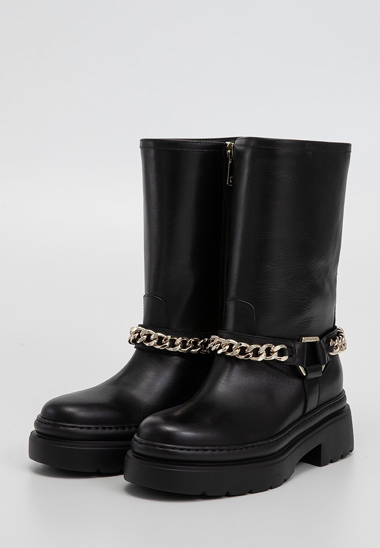 Schwarze kniehohe Stiefel aus Leder mit einer klobigen Plattform, goldenen Kettenakzenten und seitlichem Reißverschluss. Glatte Textur mit kontrastierenden Nähten.