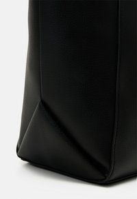Borsa in pelle nera con superficie texturizzata, forma angolare e base strutturata. Presenta bordi senza cuciture e dettagli minimi.