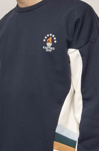 Navy blue sweatshirt with white sleeves, featuring an embroidered logo, stars, and a flame design. Includes color-blocked accents on sleeves.
