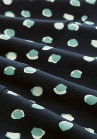 Baumwollstoff in Marineblau mit einem Muster aus unregelmäßigen Minz- und weißen Punkten, das eine weiche Textur und einen leichten Glanz durch das Gewebe aufweist.