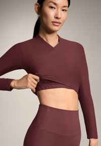Bordeauxrode longsleeve top met een wikkelontwerp, gestructureerde stof en cropped stijl, gecombineerd met bijpassende legging met hoge taille.