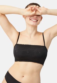Bralette de encaje negro con tirantes finos y bordes delicadamente festoneados, con una textura estampada. Tela lisa debajo en un color a juego.