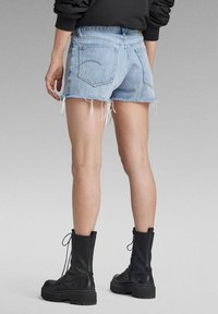 Shorts en denim bleu clair avec des ourlets effilochés, deux poches arrière et des coutures visibles. Assortis à des bottines noires avec des semelles épaisses.