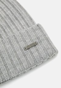 Berretto in maglia grigia con texture a coste e risvolto. Presenta un'etichetta in metallo argentato con il logo "Joop!" impresso sulla parte frontale.
