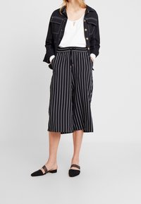 Svart och vit randiga culottebyxor med dragstring i midjan, sidofickor och en avslappnad passform. Kombinerade med en vit topp och svarta slip-on skor.