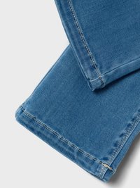 Denim tkanina v svetlo modri barvi, s kontrastnim belim šivom. Poglej bližje na hlačnice, ki prikazujejo čiste robove in gladko teksturo.