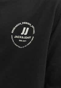 Crna majica od pamuka s bijelim otisnutim logotipom s kružnim dizajnom i natpisom: "RESEARCH_DESIGN_APPAREL JACK&JONES".