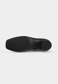 Semelle d'une chaussure habillée en cuir noir avec bout carré, motif texturé antidérapant et petit nom de marque embossé "DKNY" sur la zone de la voûte plantaire.