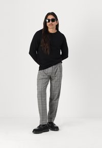 Cămașă neagră cu mâneci lungi, pantaloni gri în carouri și pantofi negri masivi. Accesorizată cu ochelari de soare închiși la culoare. Părul lung cade pe umeri.