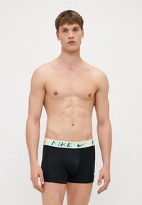 Nike crne bokserice s svijetložutim pojasom na kojem je plavo "NIKE" logo. Materijal se čini glatkim i uskim.