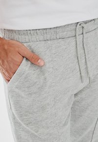 Szare bawełniane spodnie dresowe z elastycznym paskiem, bocznymi kieszeniami i miękką teksturą. Zbliżenie, które podkreśla szczegóły kieszeni i tkaniny.
